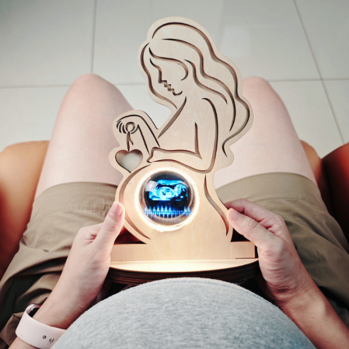 Pregnant woman holding a wooden fetus monitor with a digital display.